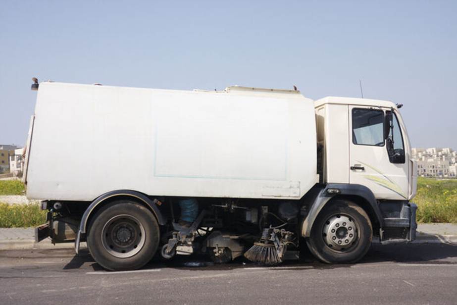 A white street sweeper truck sits on an asphalt road, ready to clean. 